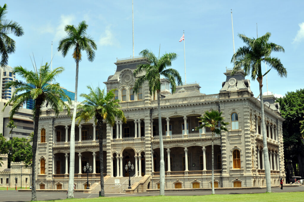 Color photo of white palace, with grass and palm trees out front
